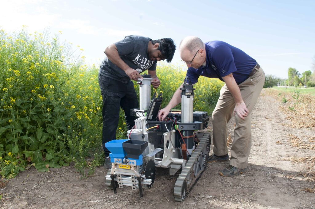 Two researchers working on a ground vehicle robot with a grain drill prototype.