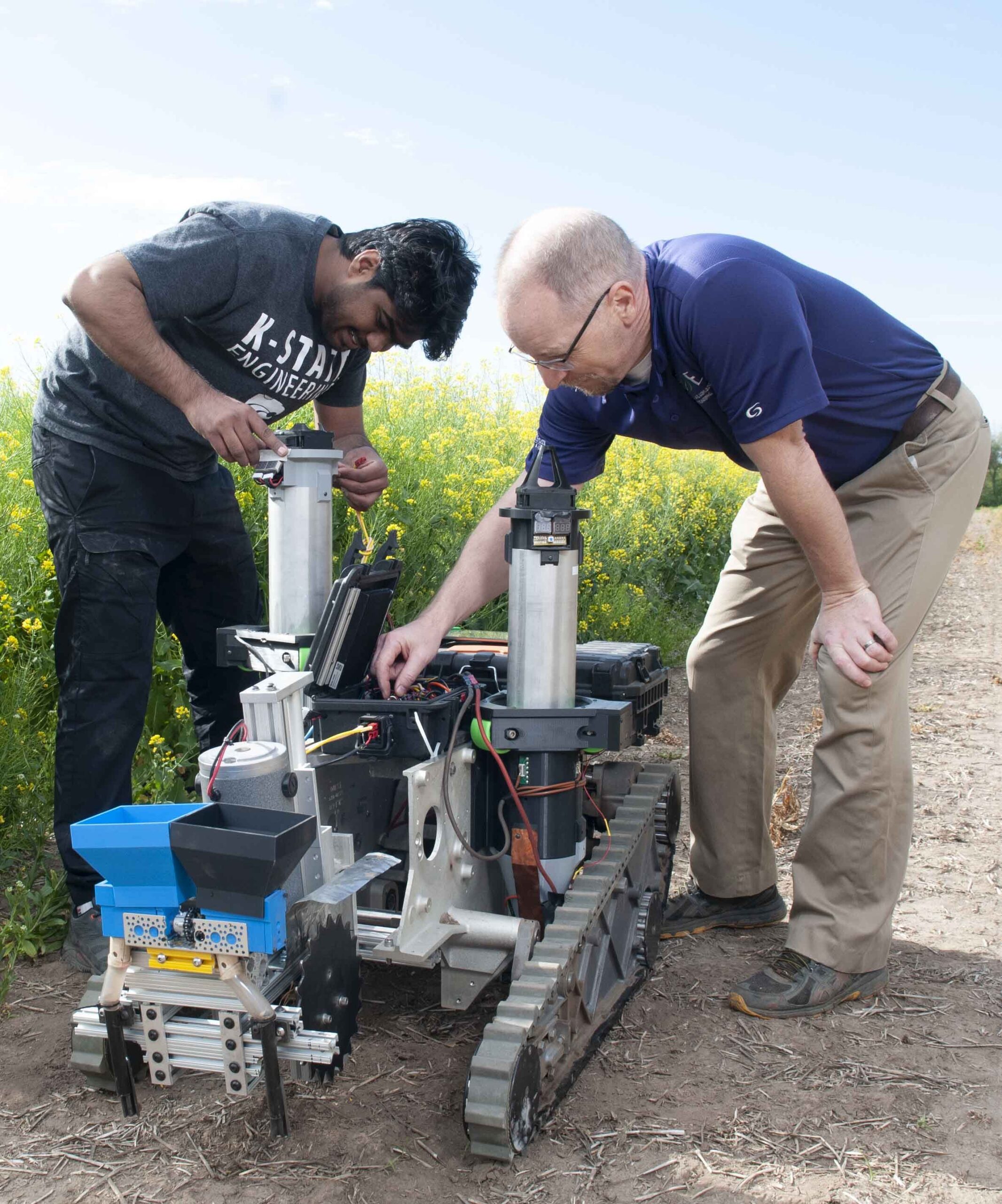 Two researchers working on a ground vehicle robot with a grain drill prototype. 